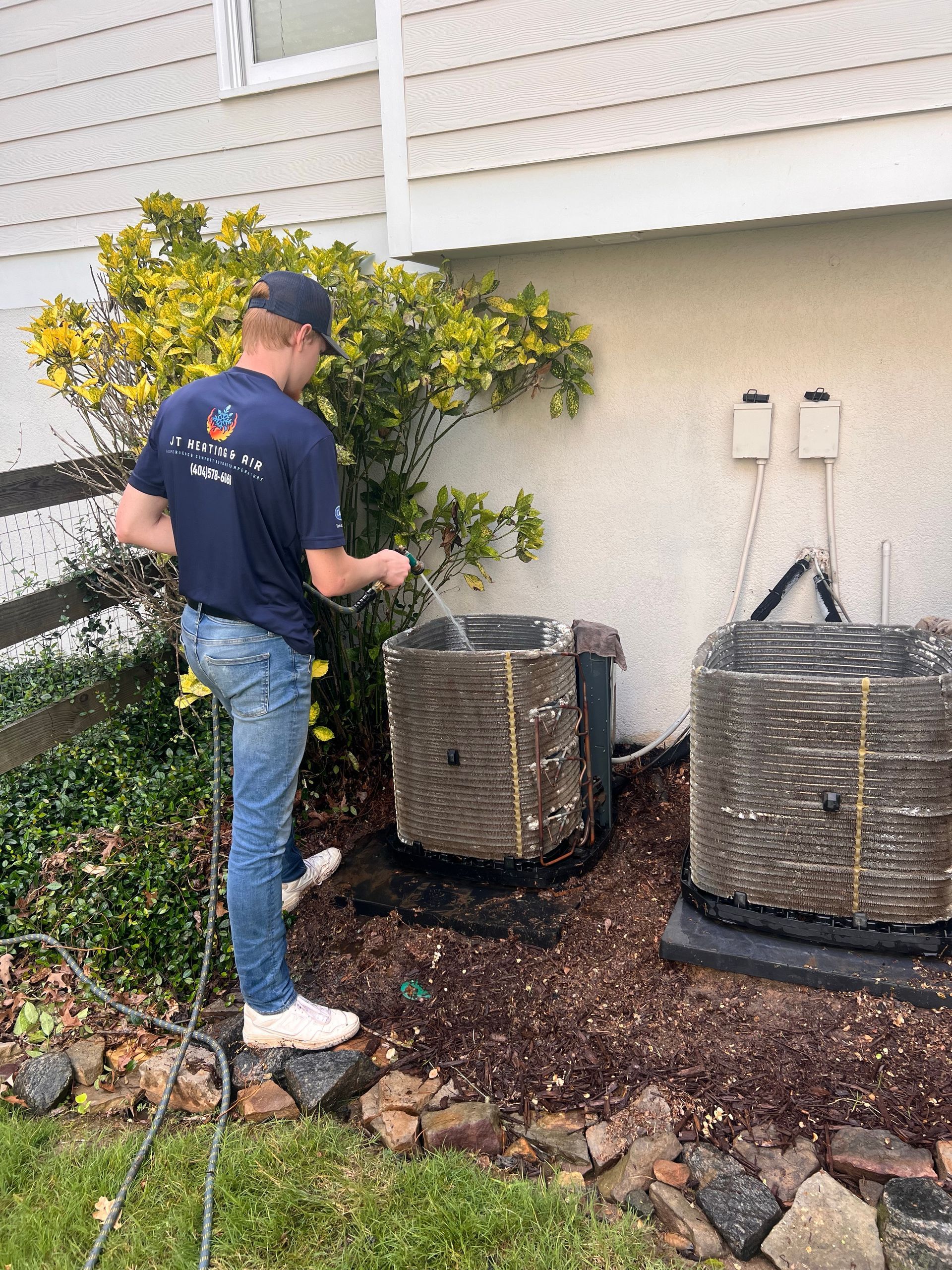 Person inspecting outdoor air conditioner units beside a house and shrubs
