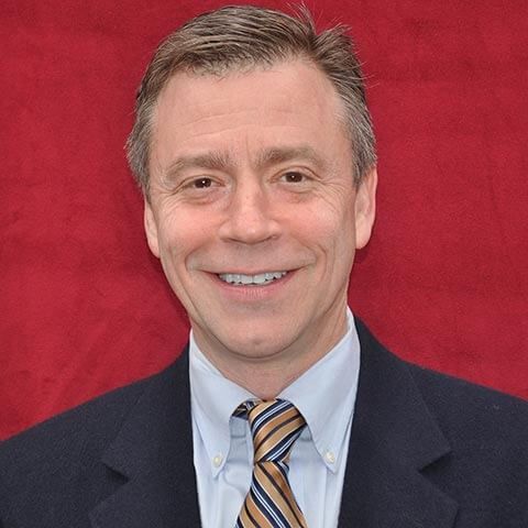 A man in a suit and tie is smiling in front of a red background