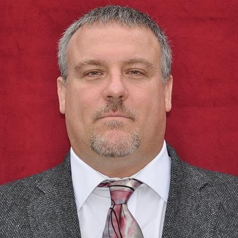 A man in a suit and tie is standing in front of a red background.