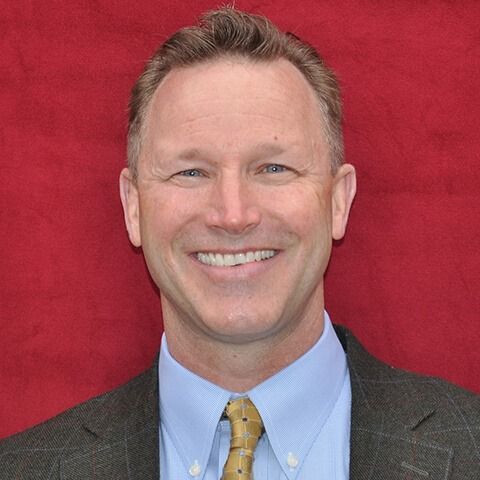 A man in a suit and tie is smiling in front of a red background