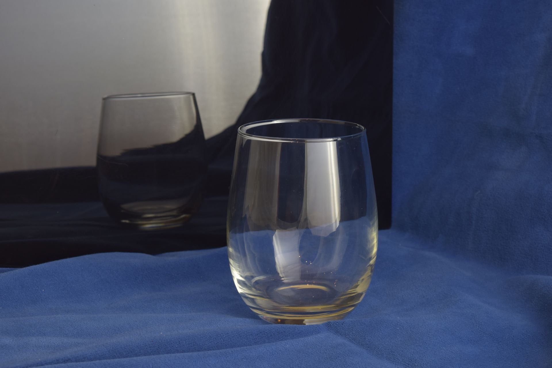 Two clear, stemless glasses on a blue cloth surface, with a dark blue backdrop.
