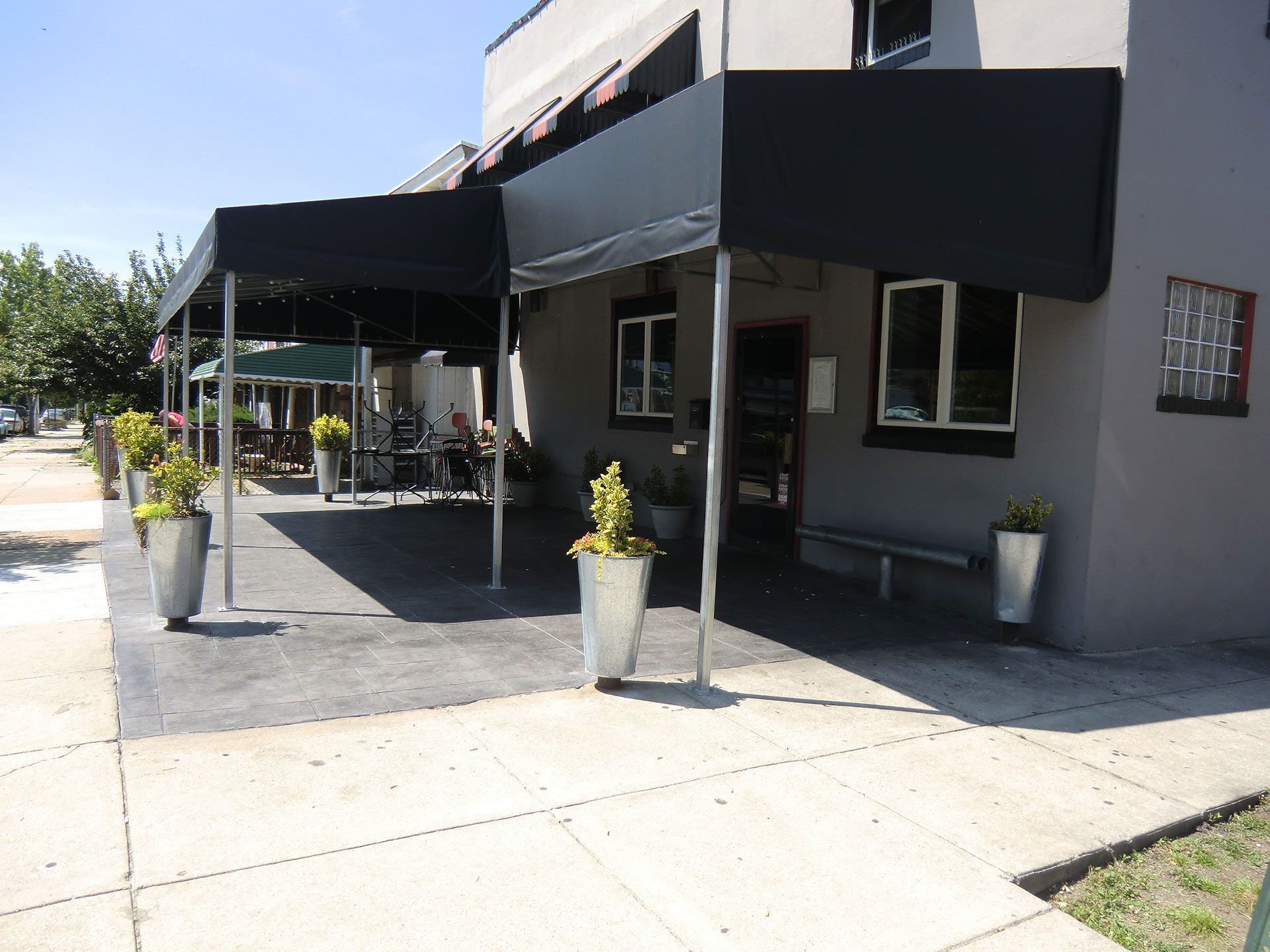 Restaurant exterior with black awnings, outdoor seating, and potted plants.