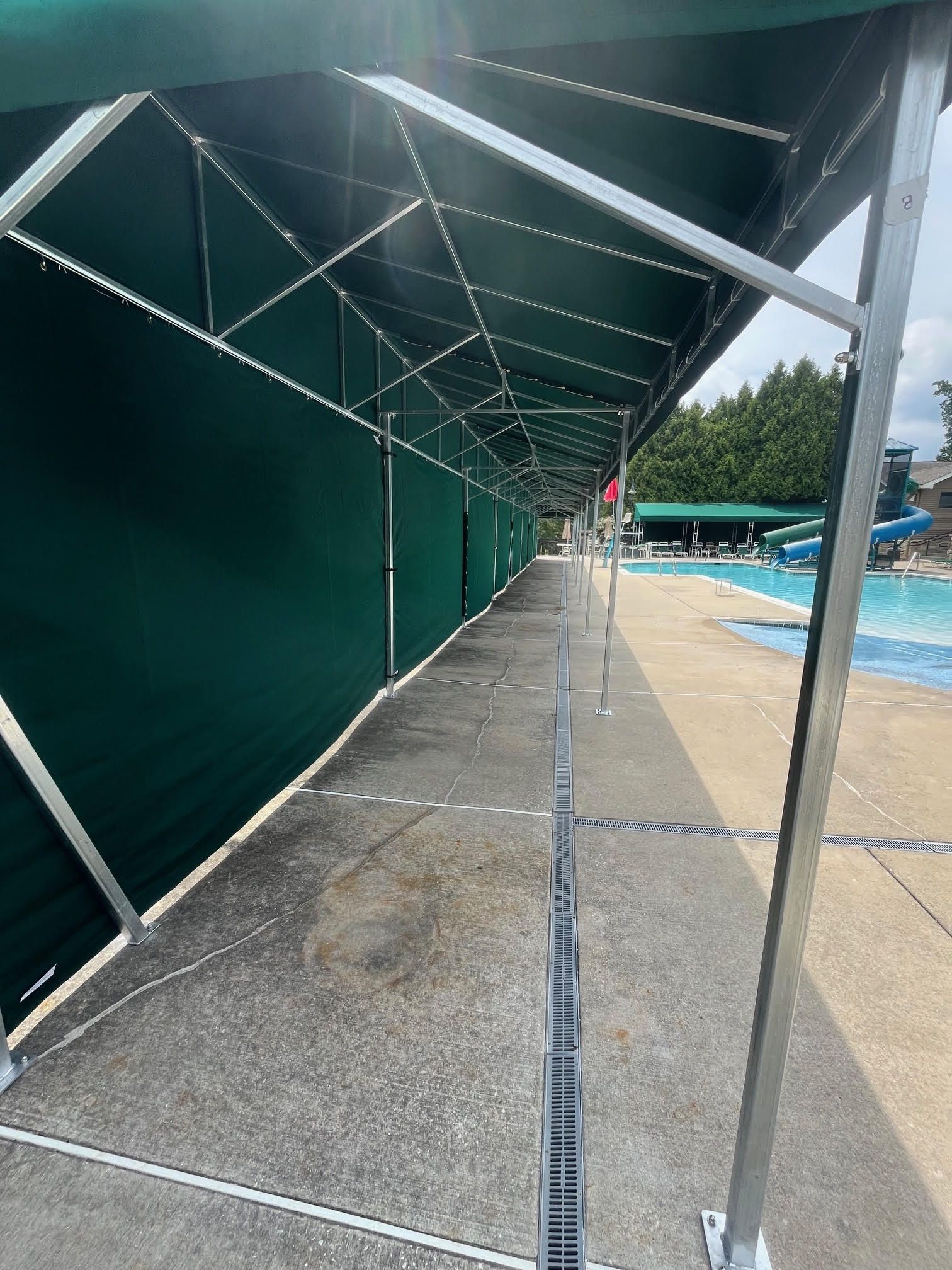 Green awning over a concrete walkway, next to a swimming pool on a sunny day.