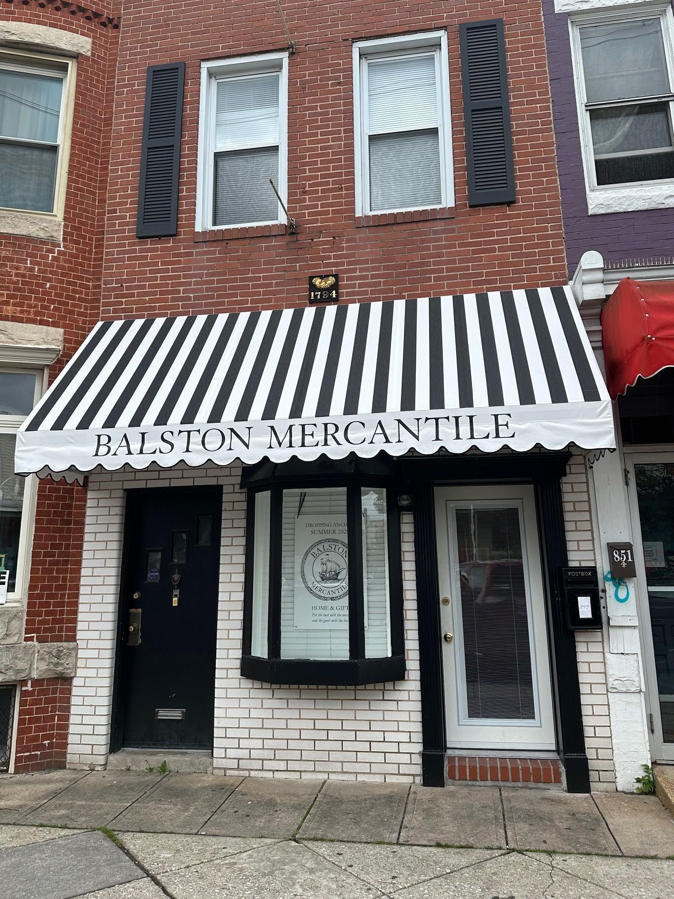 Balston Mercantile storefront with striped awning, black door, brick building, and closed shutters.