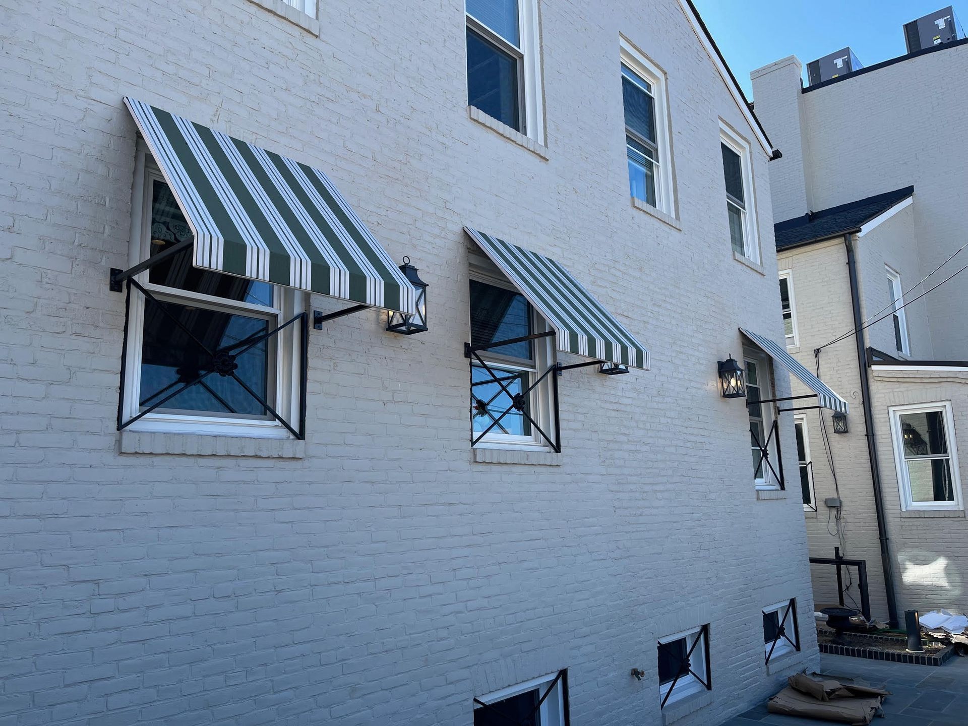 A pale gray brick building with green and white striped awnings over several windows.