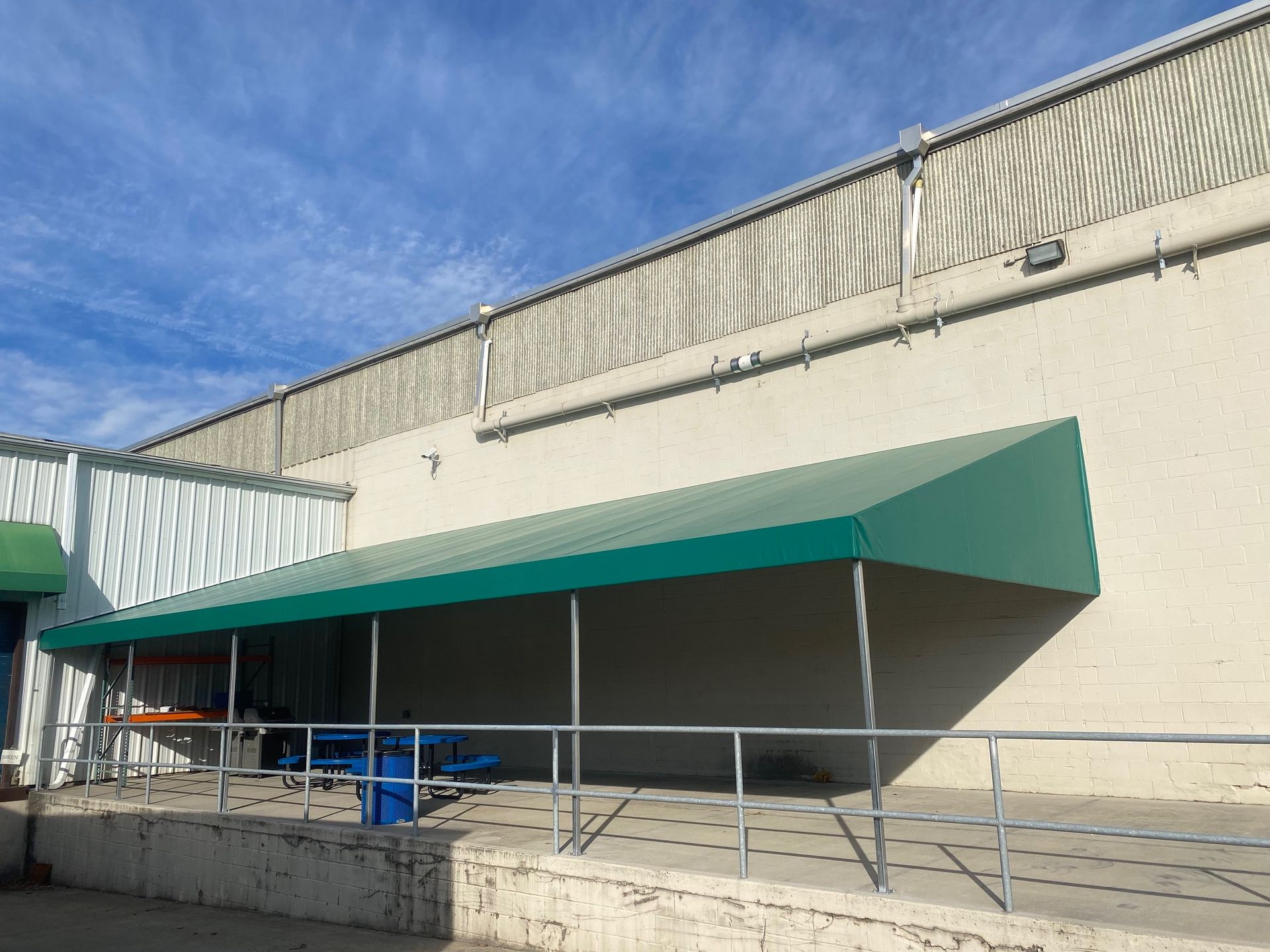 Green awning over a ramp, next to a building with corrugated metal siding, blue sky.