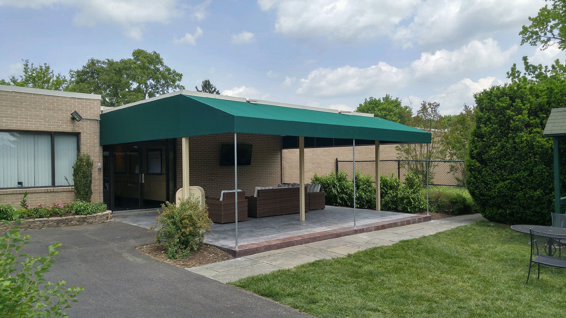 Green awning over a patio with wicker furniture, brick edging, and a grassy yard.