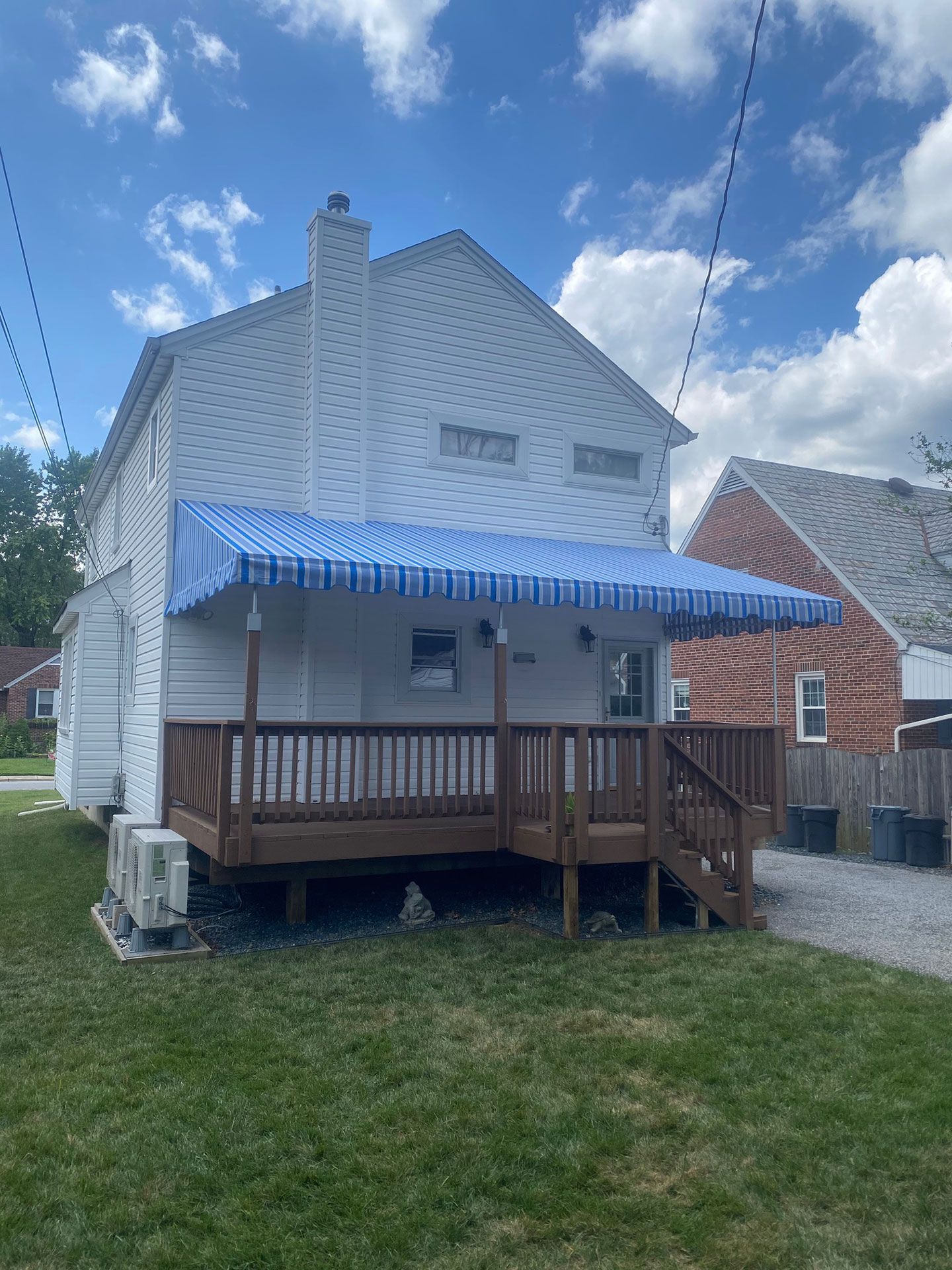Two-story white house with a blue and white striped awning over a wooden porch; green grass in front.