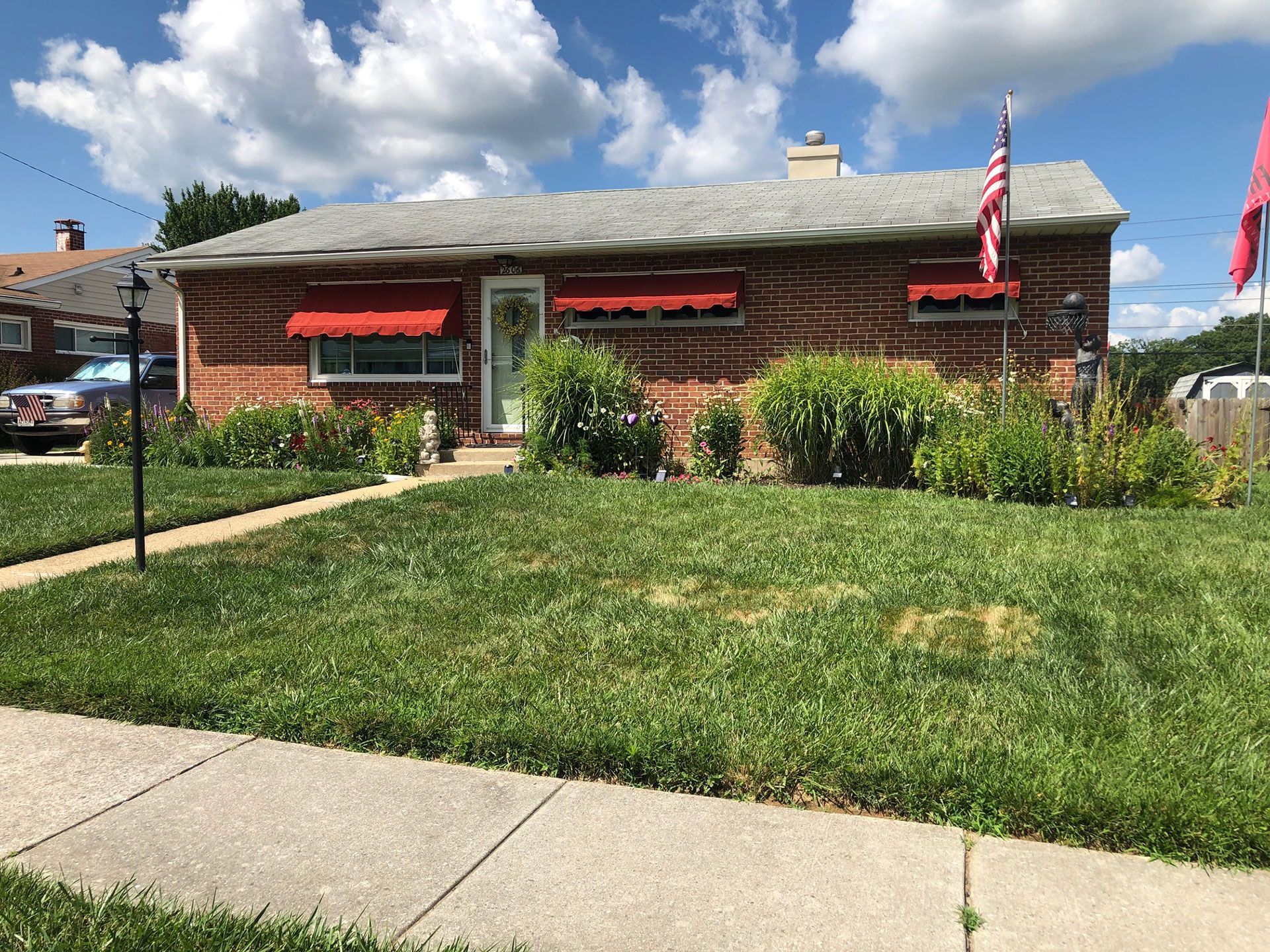 Brick house with red awnings, green lawn, and American flags on a sunny day.