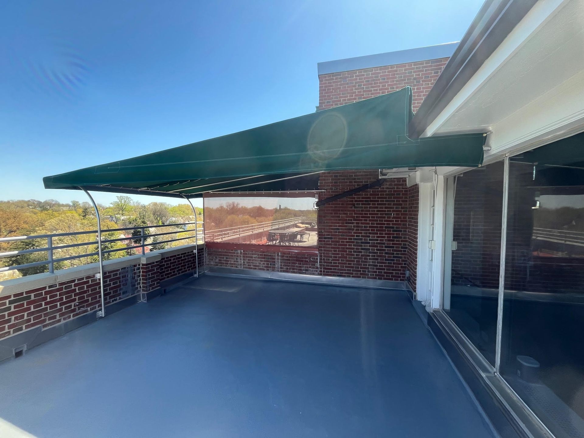 Rooftop deck with green awning, brick walls, and glass windows overlooking a cityscape.