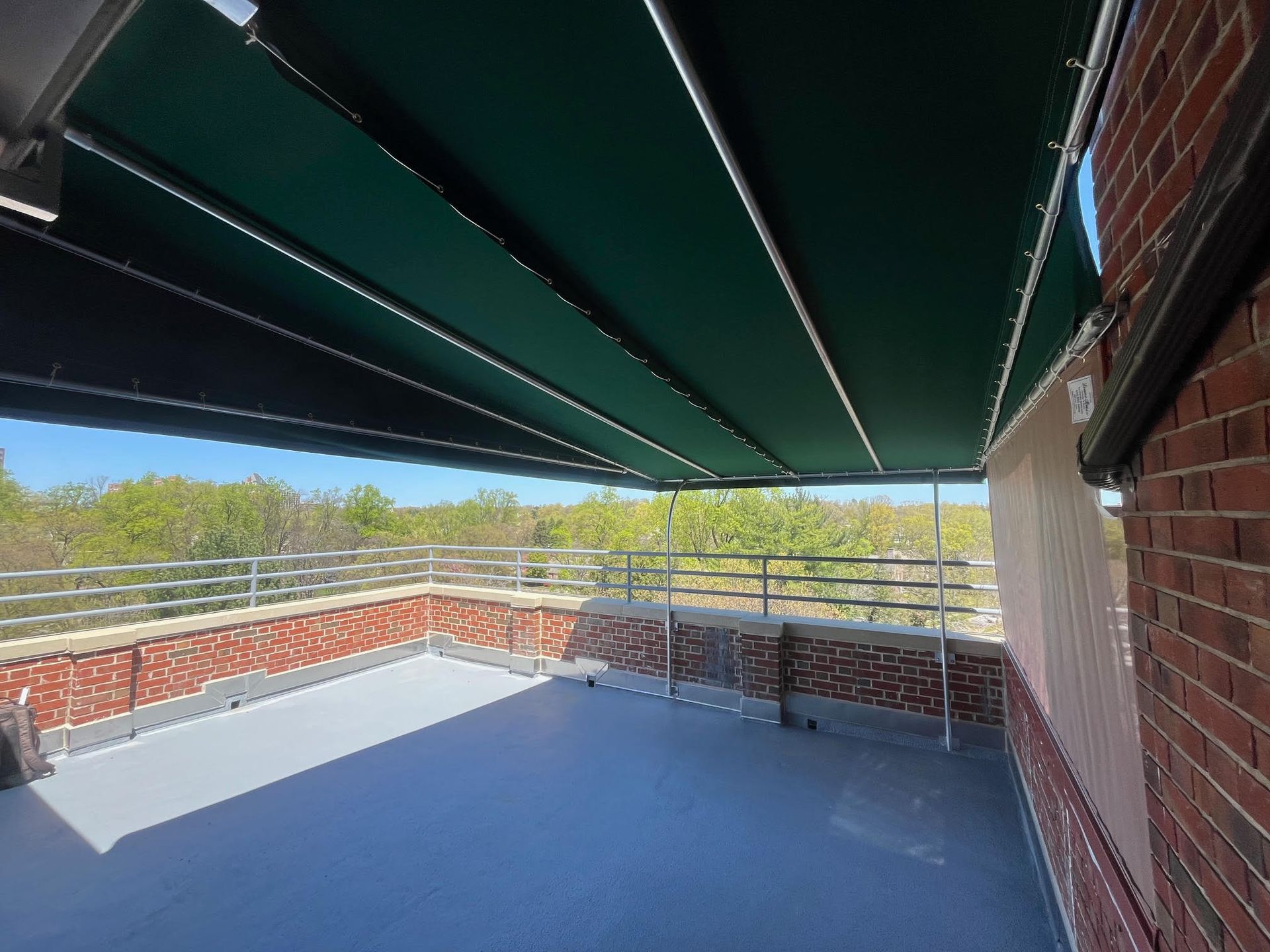 A shaded outdoor patio with retractable green awning, brick wall, and metal railing.