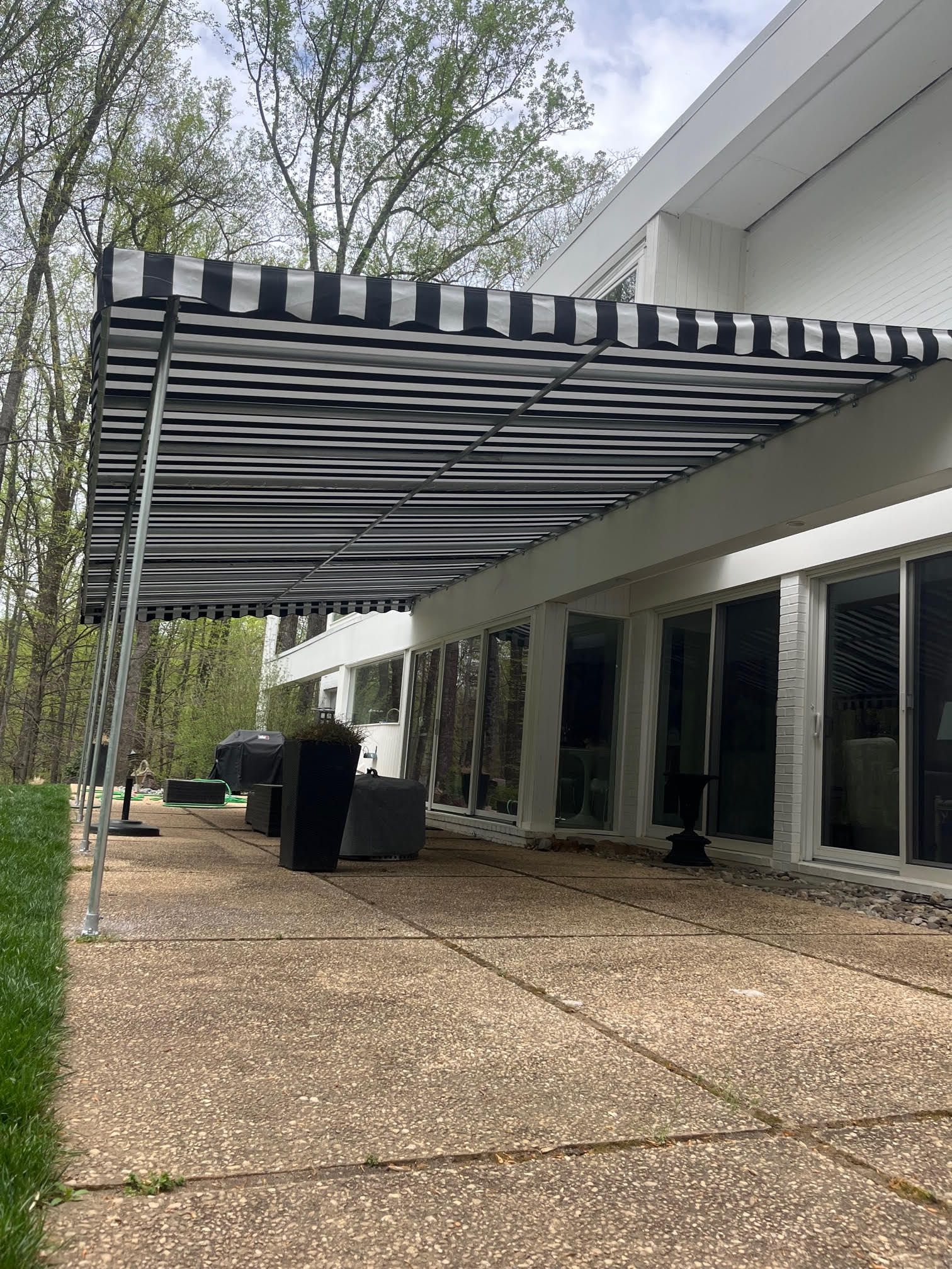 Black and white striped awning covers a patio. White house with large windows in the background.