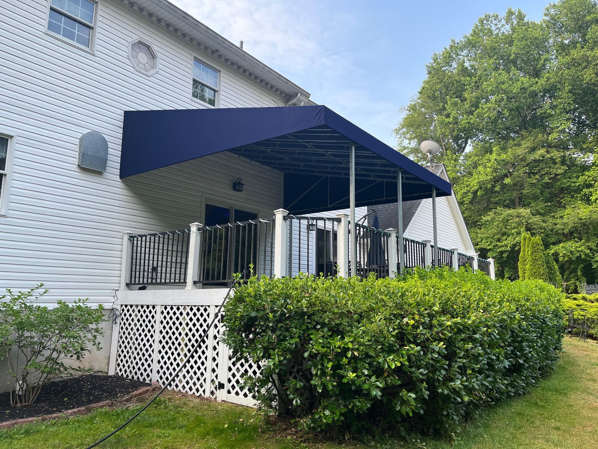 A navy blue awning covers a deck with black railings and white lattice, attached to a white house.