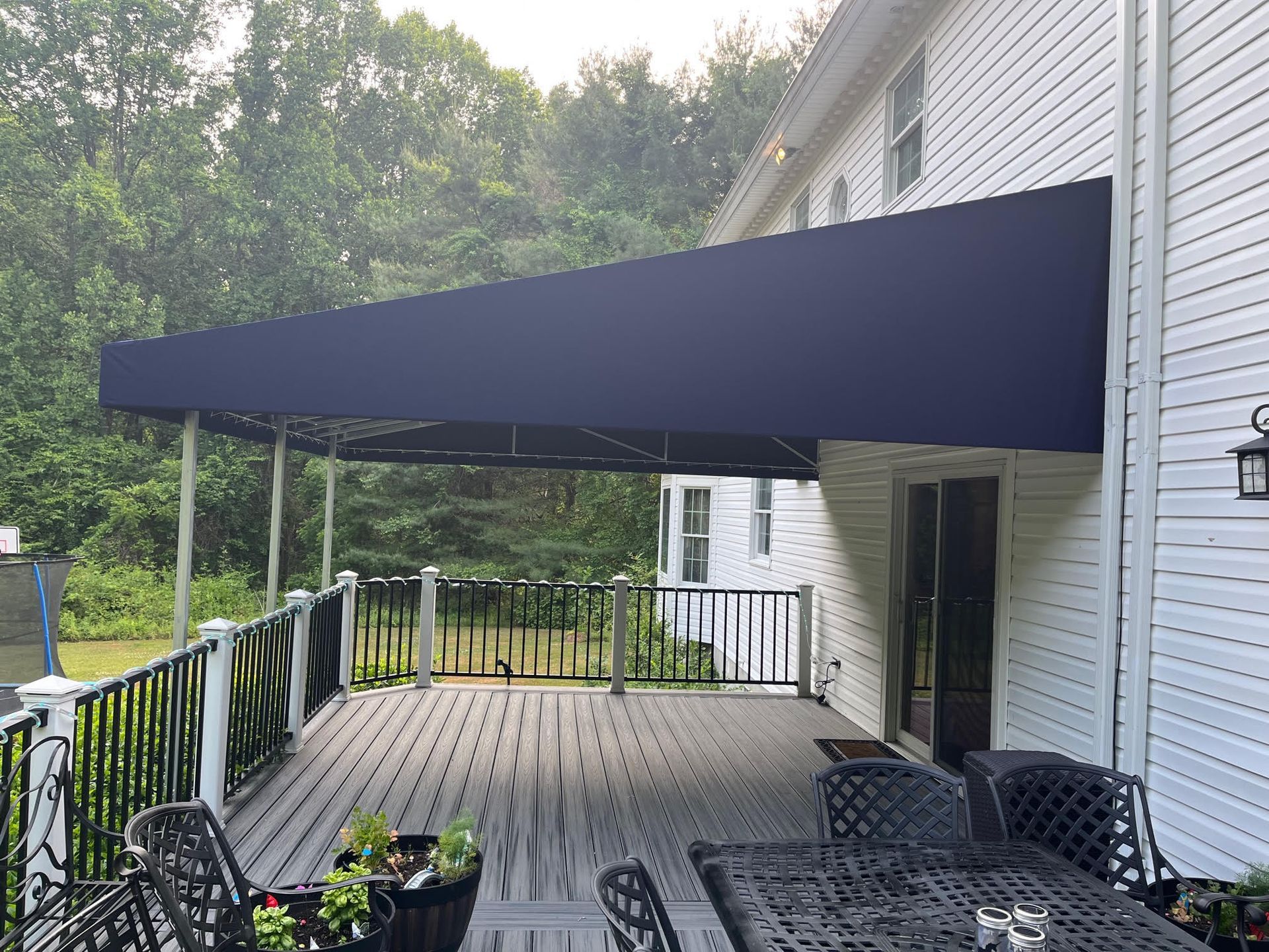 Blue awning over a wooden deck with black railings, against a white house.