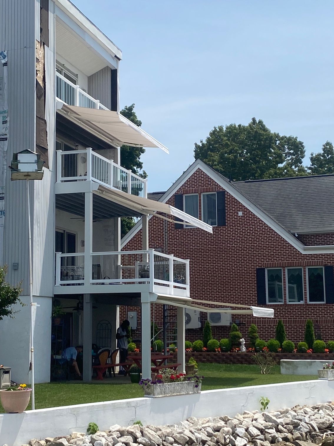 Multi-story building with white decks, retractable awnings, and glass railings, with a brick building in the background.