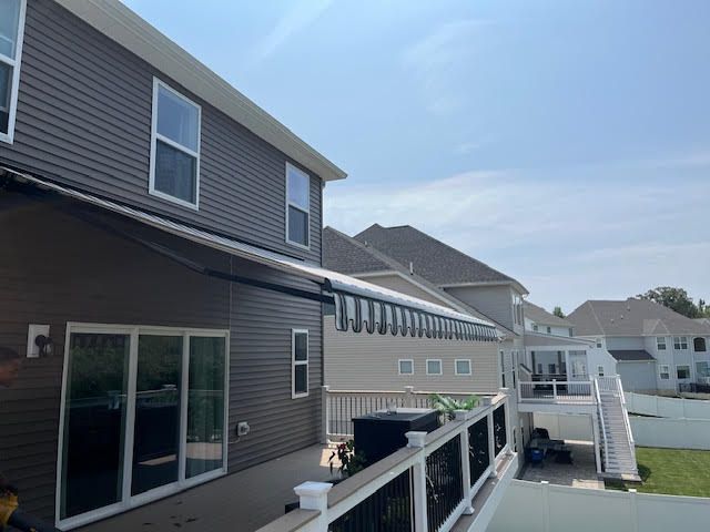 Dark brown house with deck, awning, and glass sliding doors; sunny day.