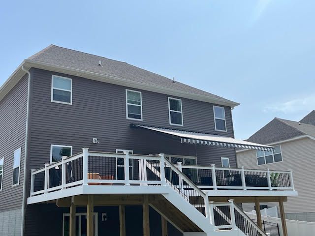 Back of a two-story house with a deck. Brown siding, white trim. Deck has stairs and awning. Blue sky.