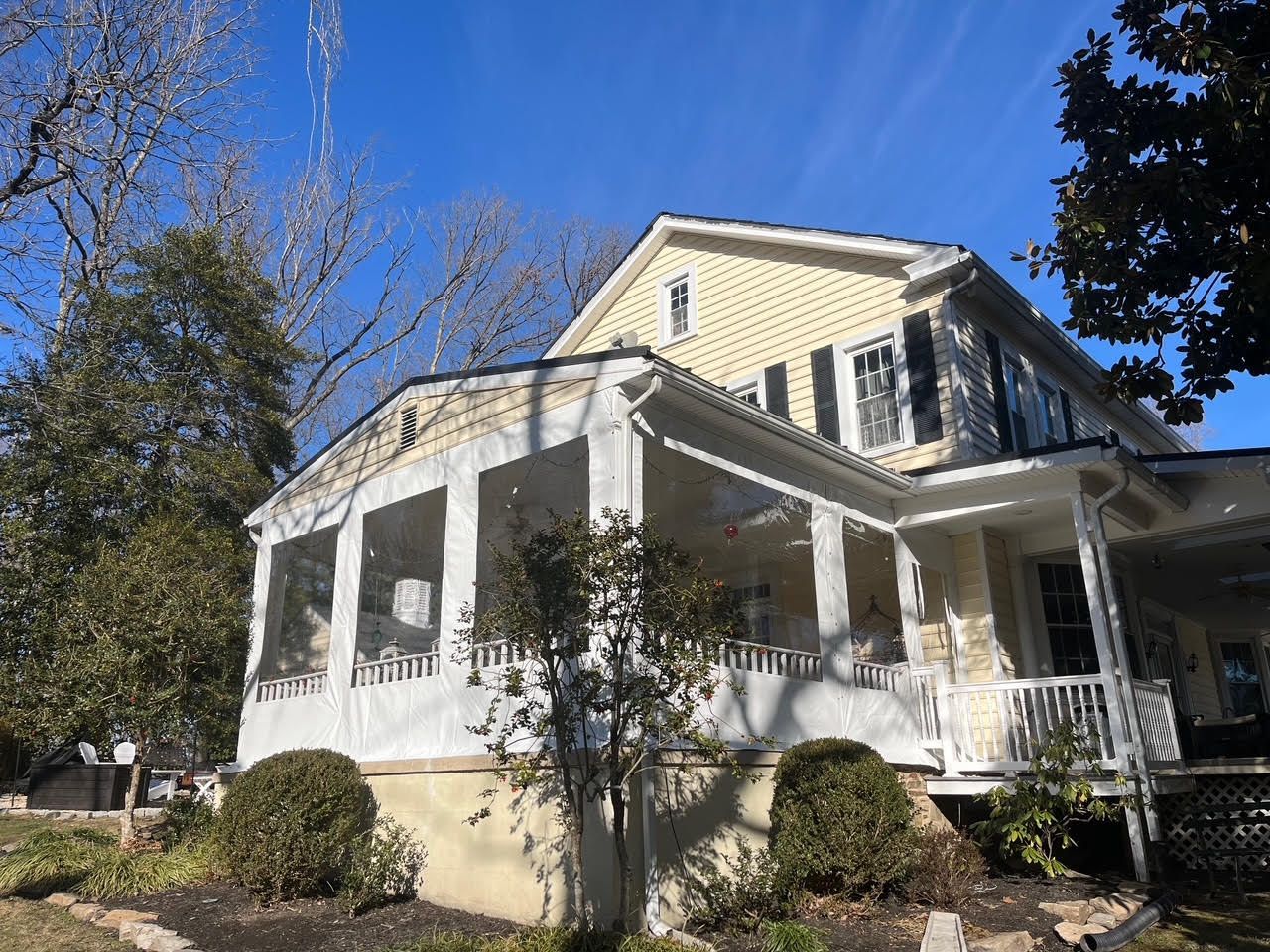 Yellow house with a wraparound porch, screened with white fabric, under a blue sky.