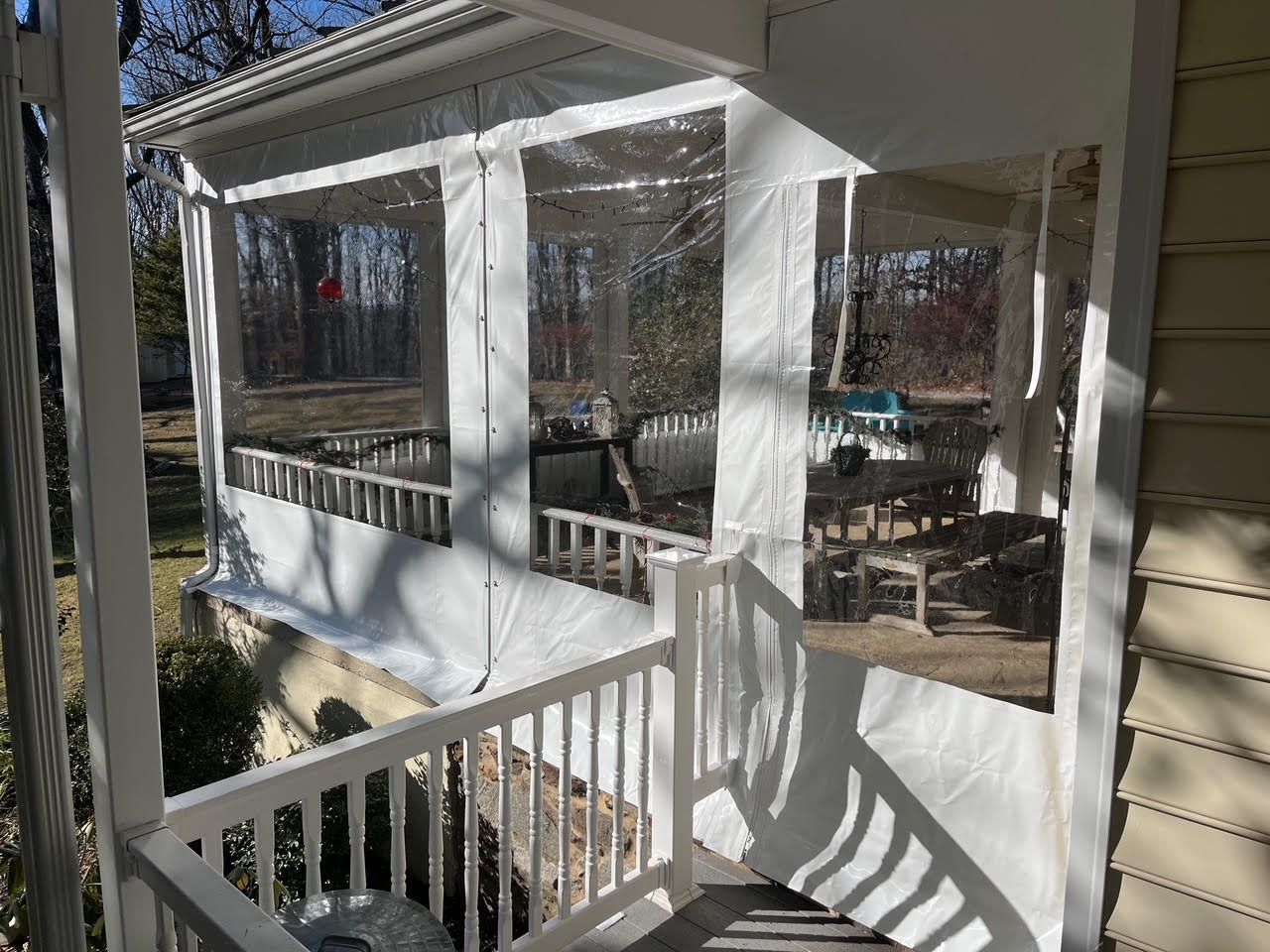 Enclosed porch with clear plastic panels, white railings, and outdoor furniture visible.
