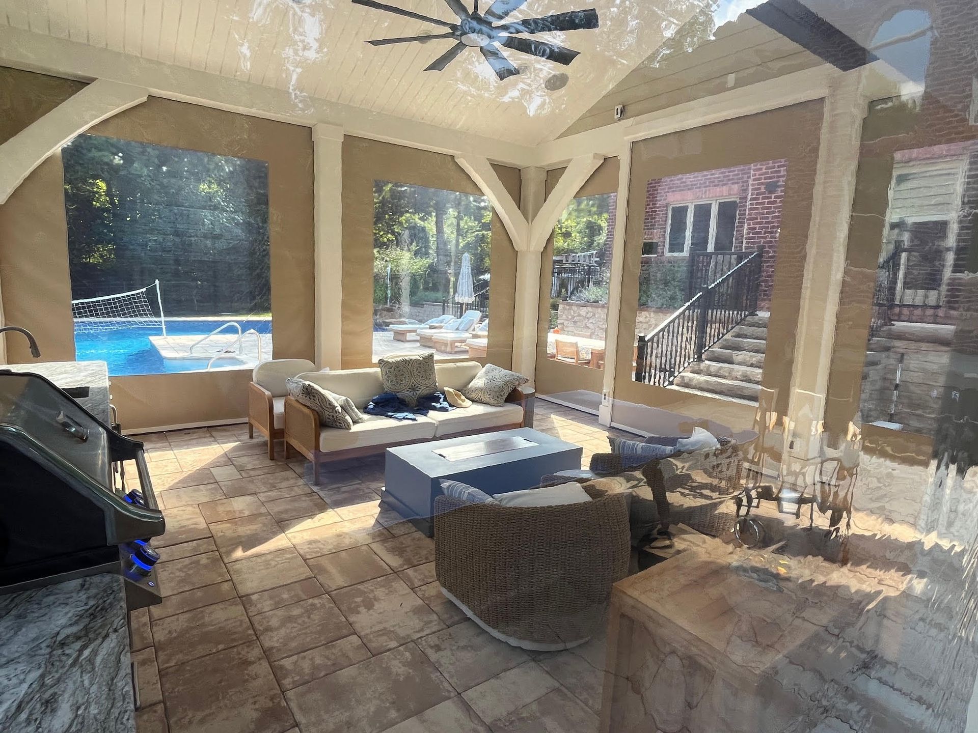 Enclosed patio with furniture, views of a pool and house, neutral tones, and a ceiling fan.