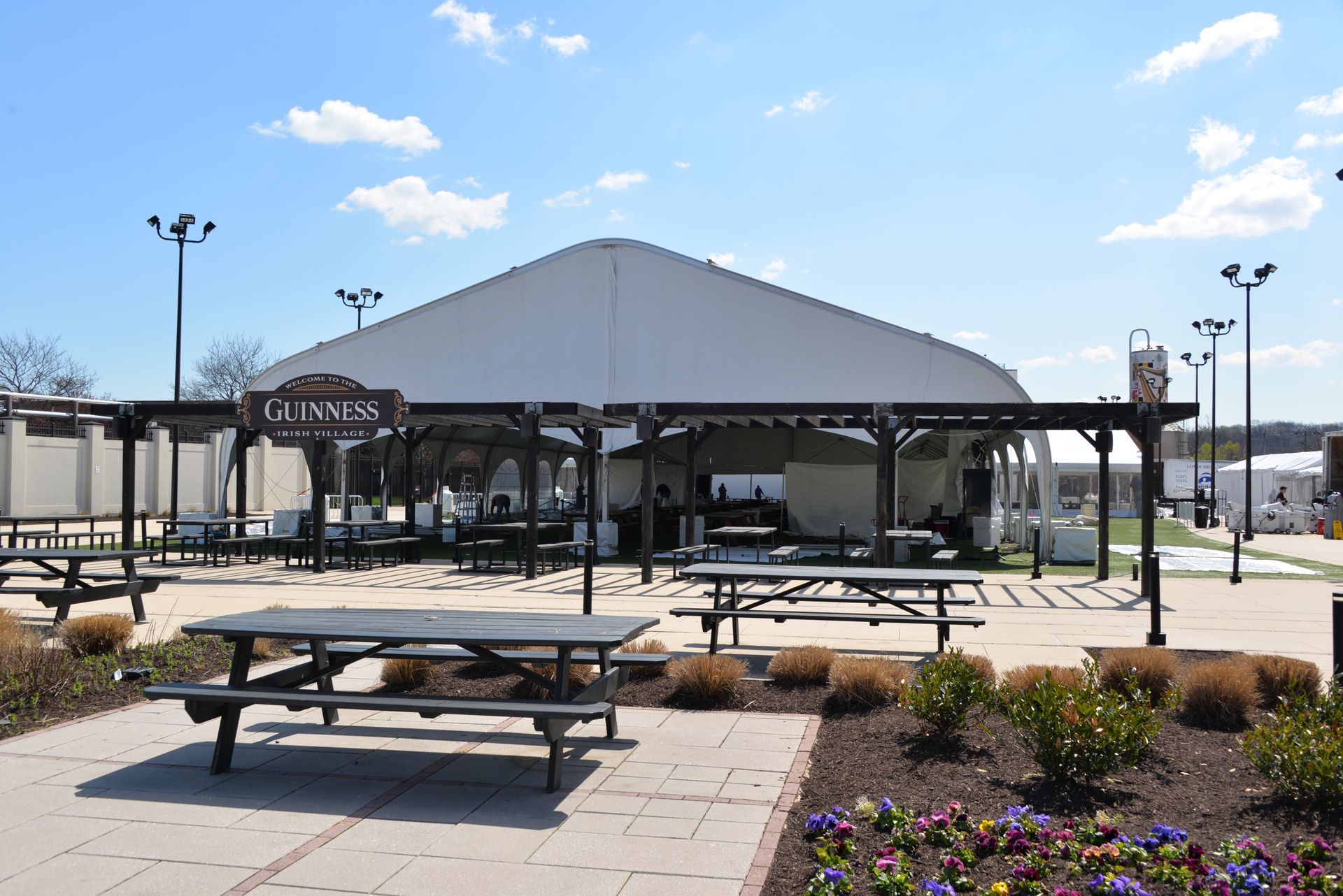 Outdoor seating area with picnic tables, a pergola, and a large white tent.