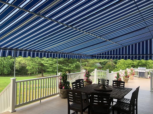Deck with blue and white striped awning, dining set, overlooking green trees and lawn.