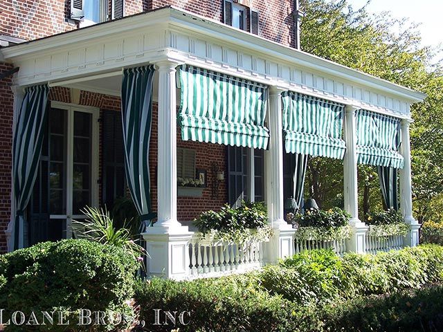 White porch with green-striped awnings and curtains on a brick building.
