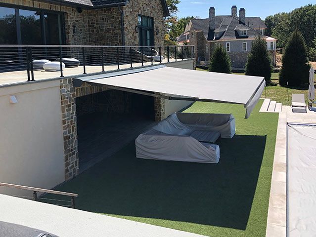 Covered outdoor seating area under a retractable awning, stone building with a pool in the background.
