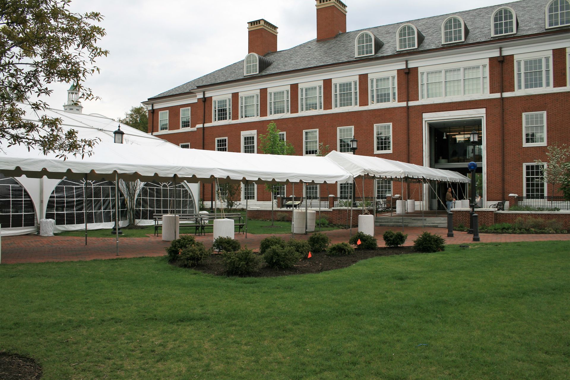 White tents outside a red brick building. Grass lawn in the foreground. Overcast sky.