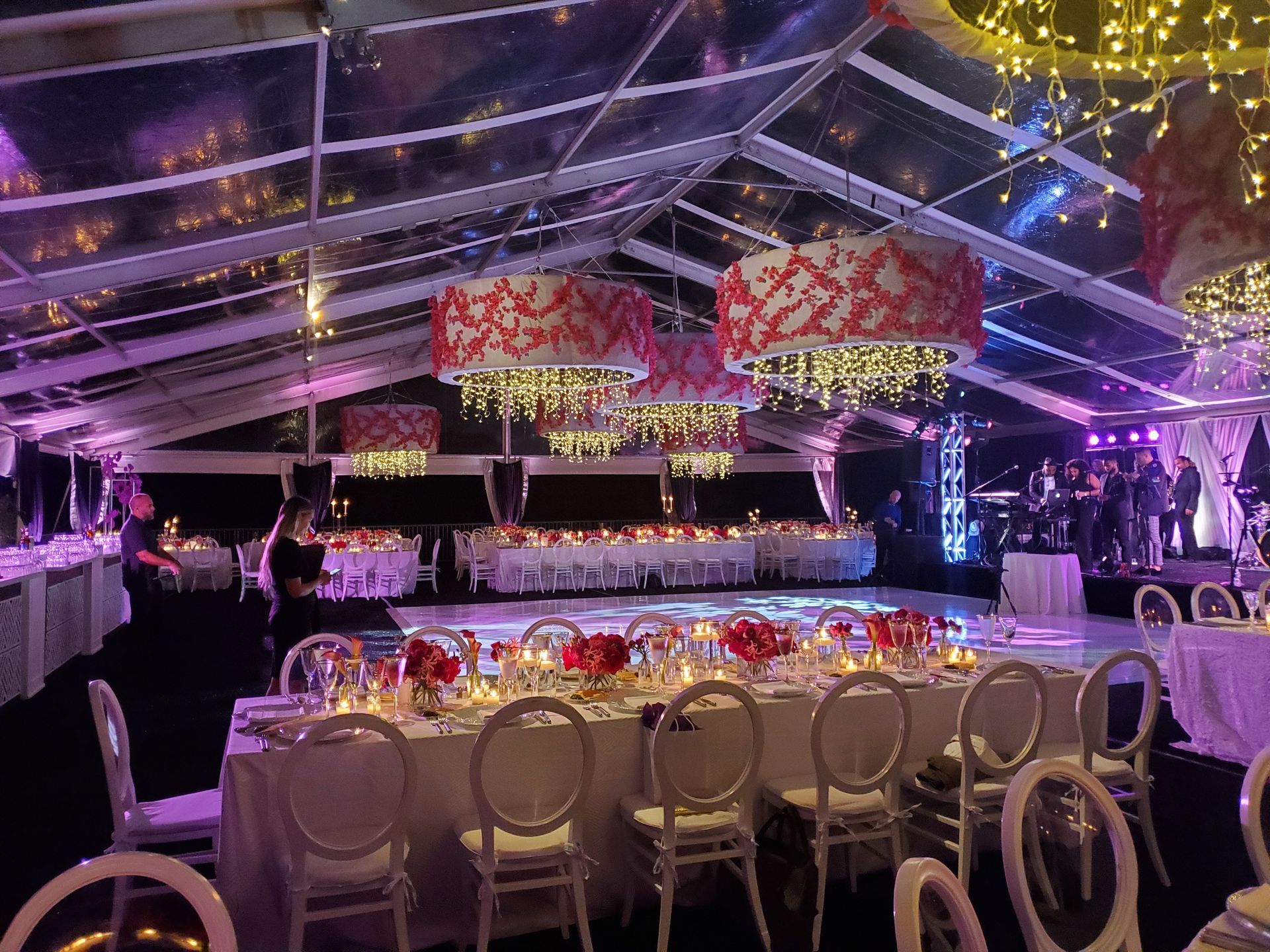 Elegant wedding reception under a clear tent, with tables, decorations, and a dance floor.