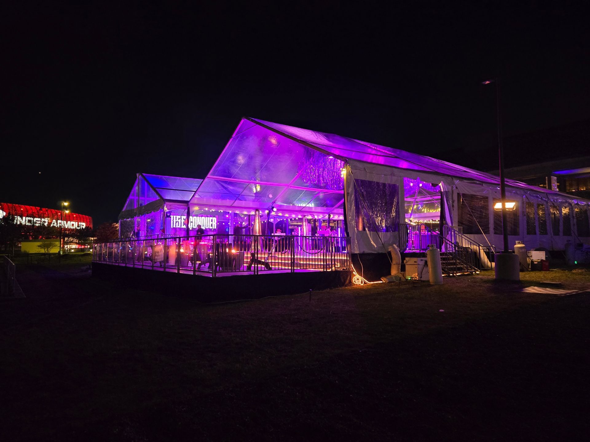 A clear tent lit with purple lights at night, with tables and people inside.