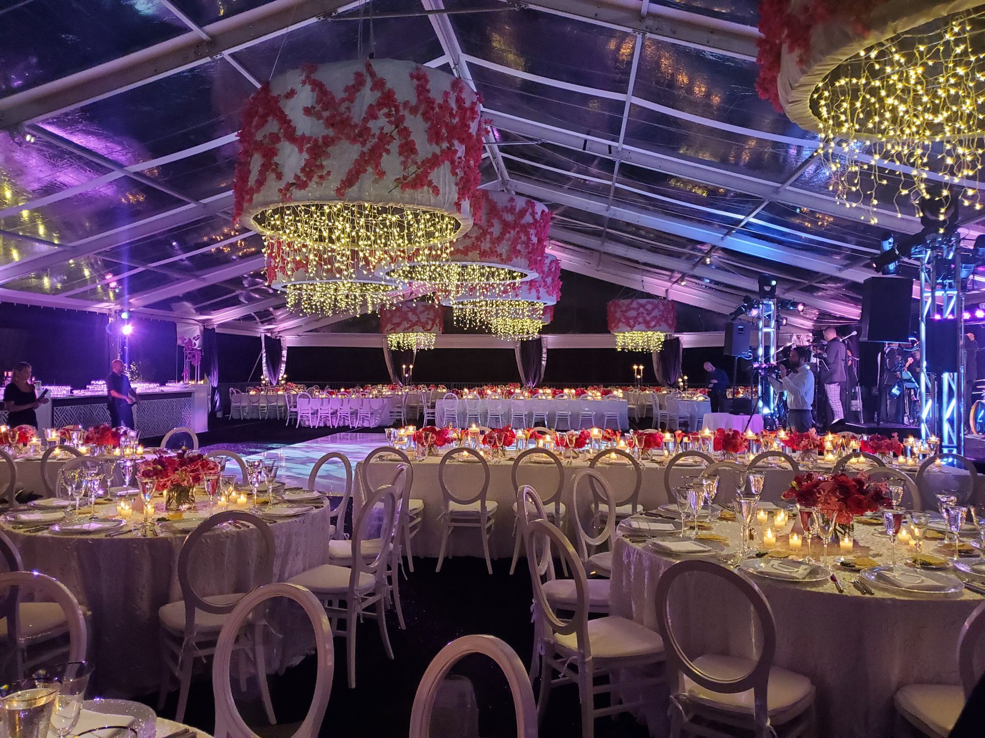 Elegant event tent with round tables, chandeliers, and a stage, lit in purple and gold.