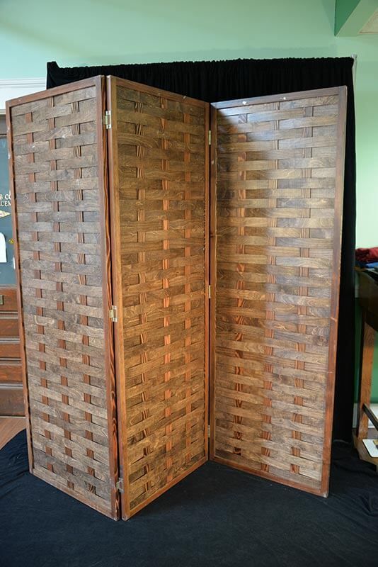 Three-panel wooden screen with woven-patterned panels, brown frame, placed indoors.