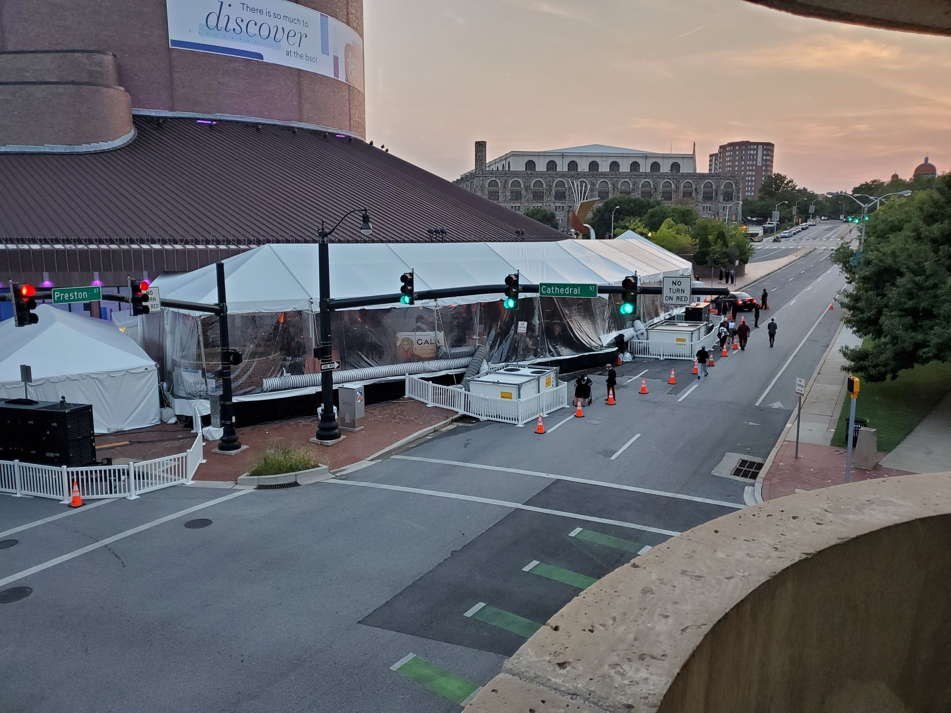 Event tent set up on a street with a large building on the left, people walking, and an evening sky.