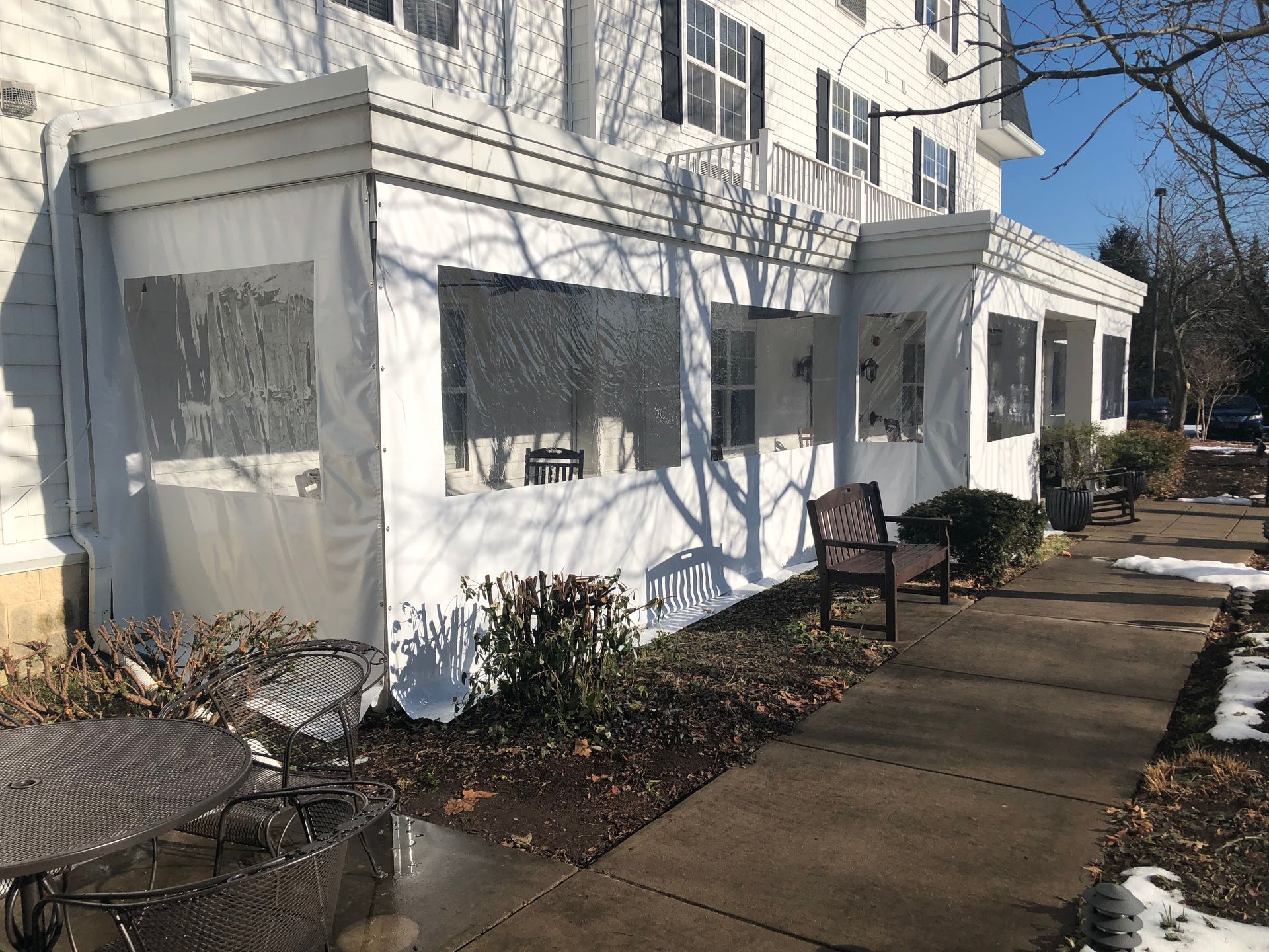White awning with clear windows over a building entrance, a bench, and a walkway with snow.