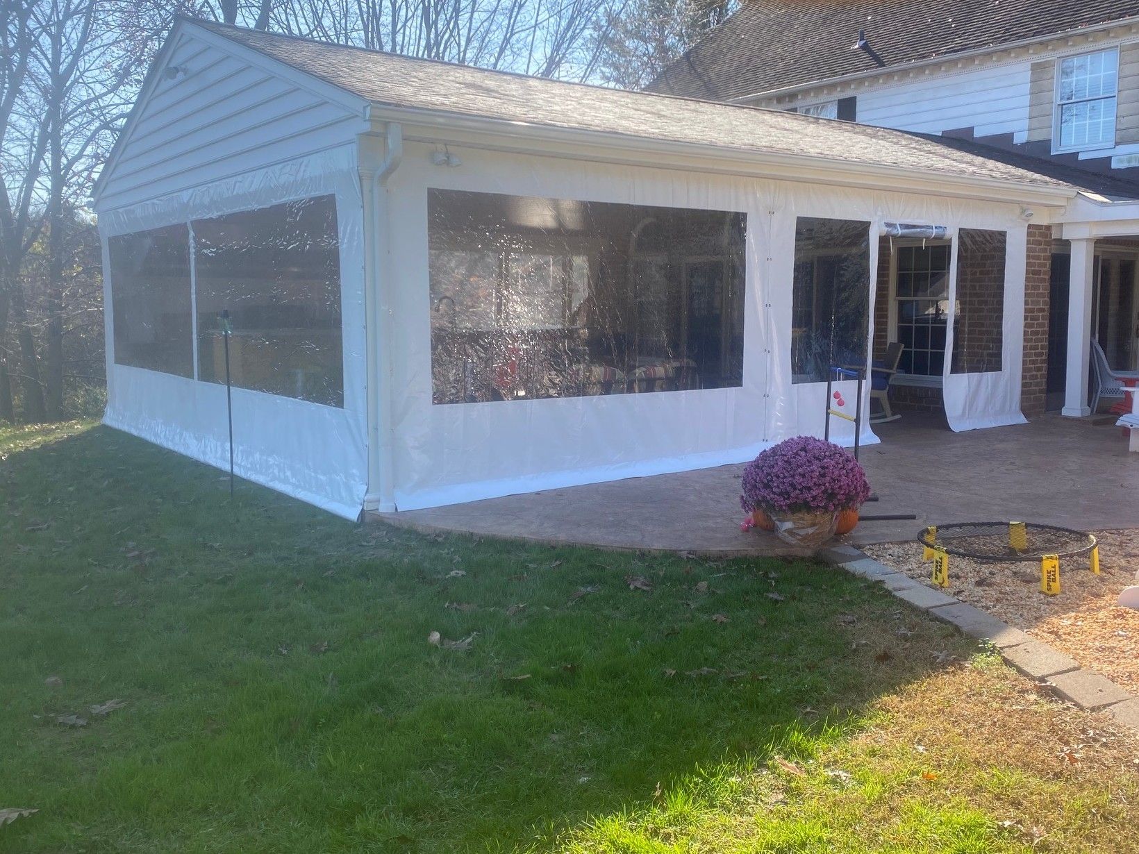 Enclosed patio with clear vinyl panels, white trim, attached to a brick house, on green lawn.