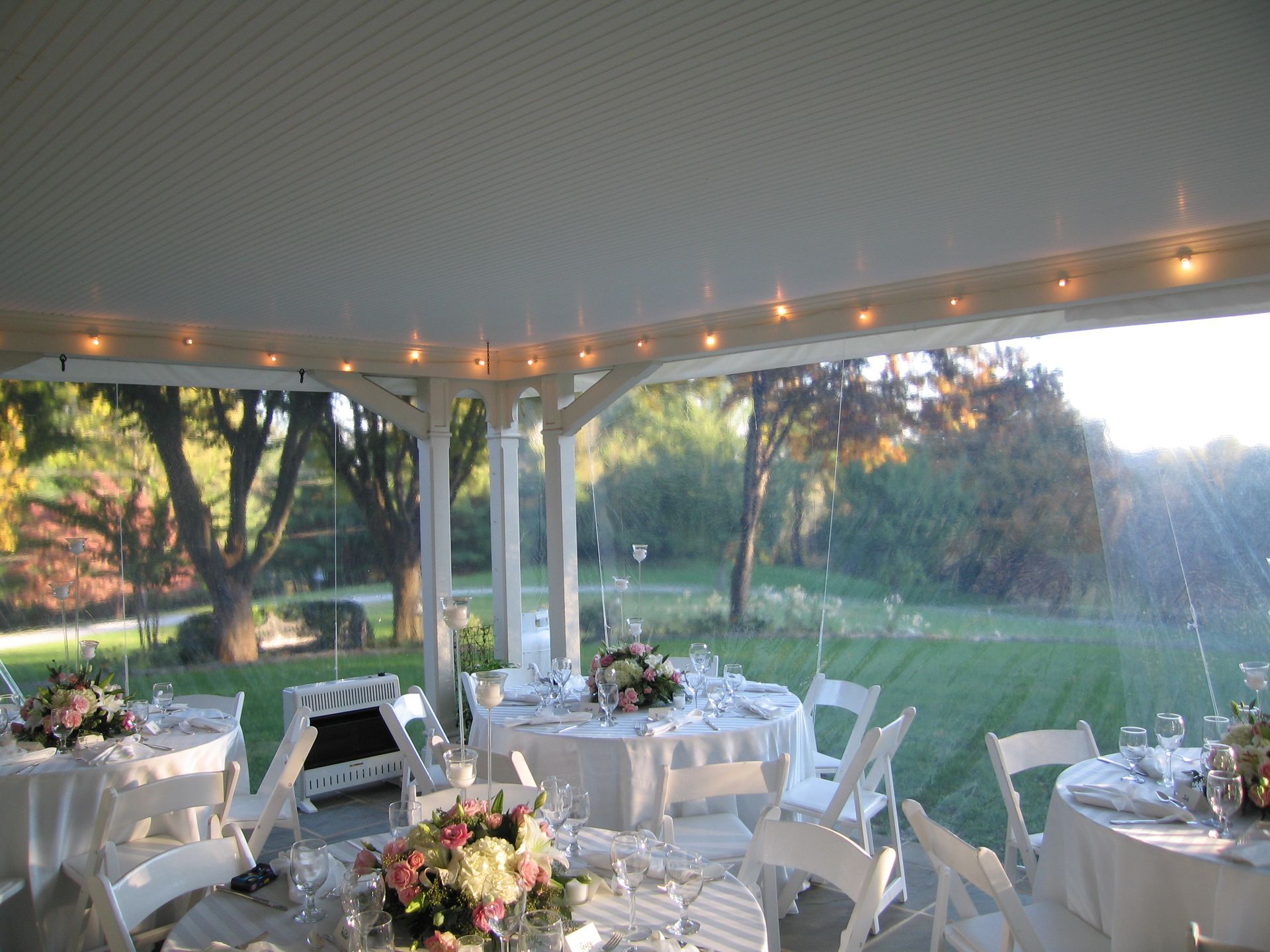 Outdoor wedding reception, tables set under a white canopy, rain falling in the background.