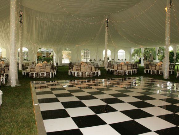 A black and white checkered dance floor in a tent with round tables and chairs set up for an event.