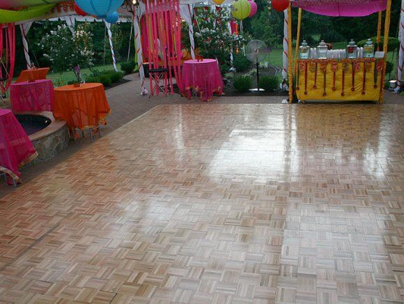 Wooden dance floor with colorful decorations in the background at an outdoor event.