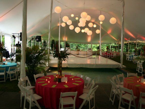 A brightly lit outdoor tent with tables, chairs, and a dance floor, decorated for an event.