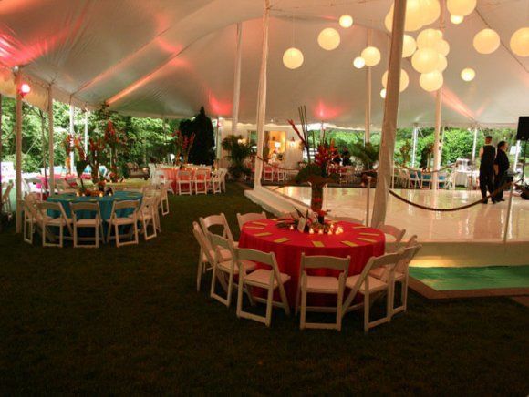 Event tent with round tables, white chairs, and paper lanterns. Green lawn, dance floor.