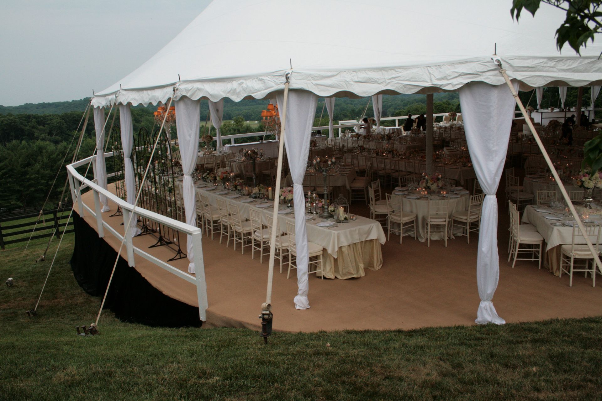 White tent on a wooden platform overlooking a landscape with tables and decorations inside.