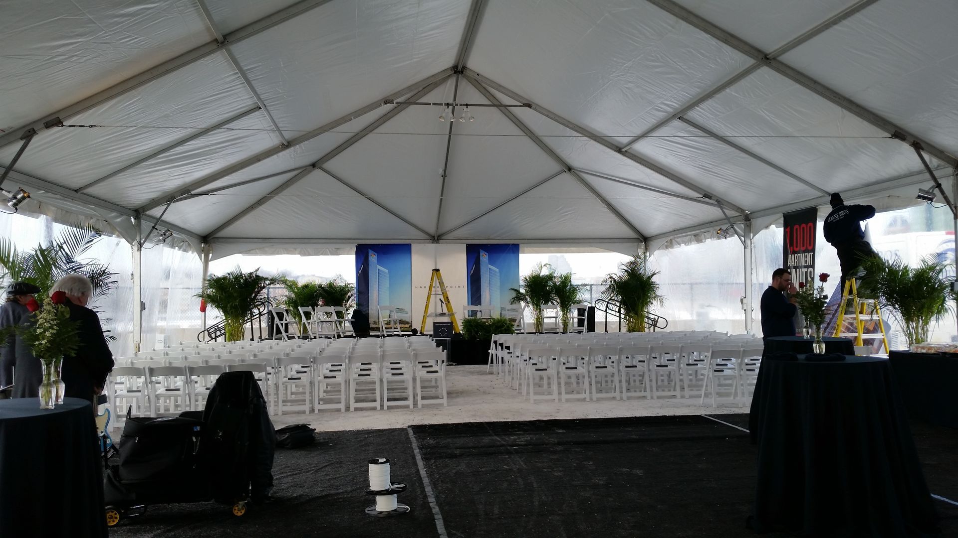 Inside a large white tent, rows of white chairs face a stage with blue banners.