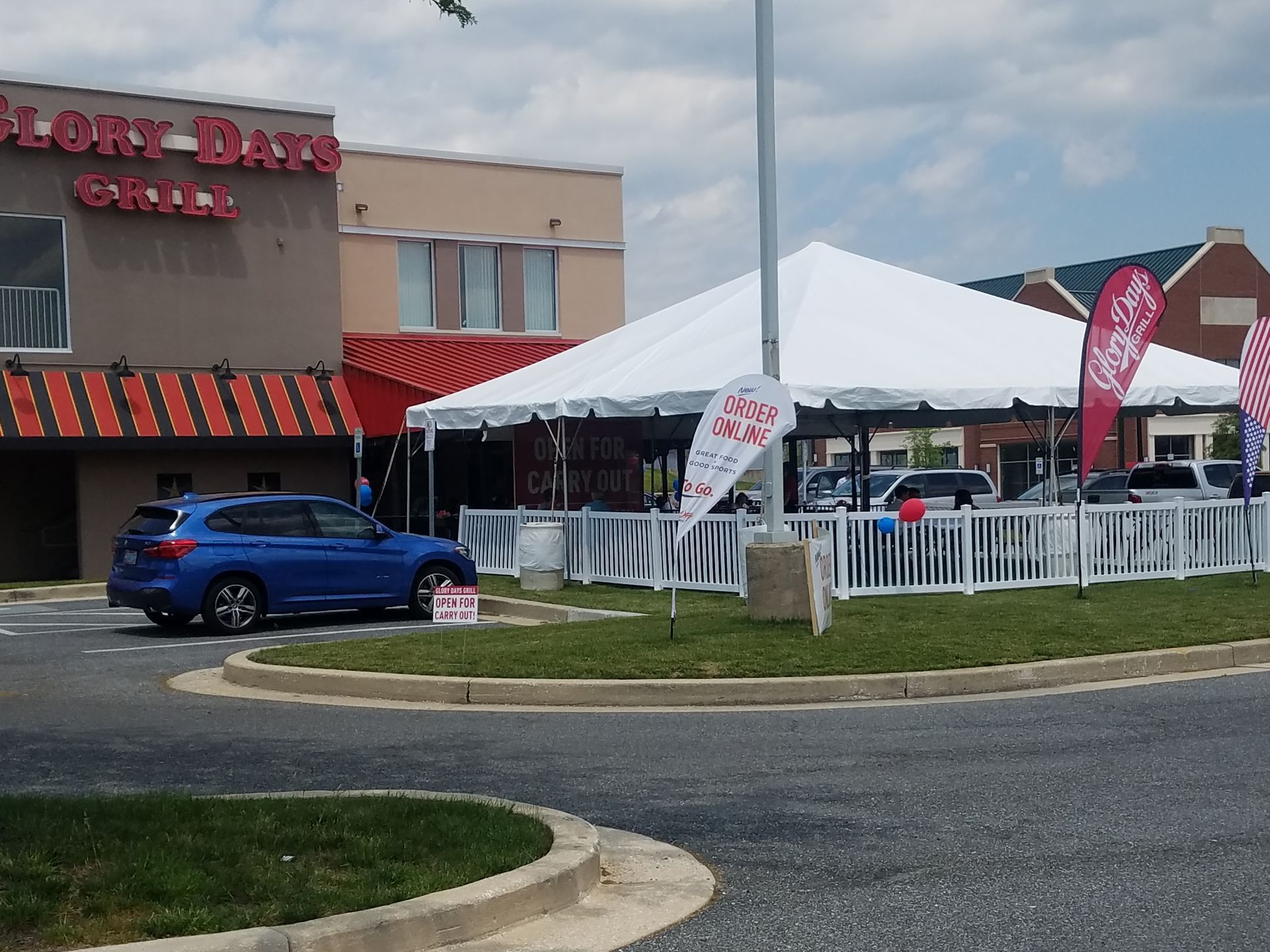 A blue car parked in front of Glory Days Grill, with a white tent set up for outdoor dining.