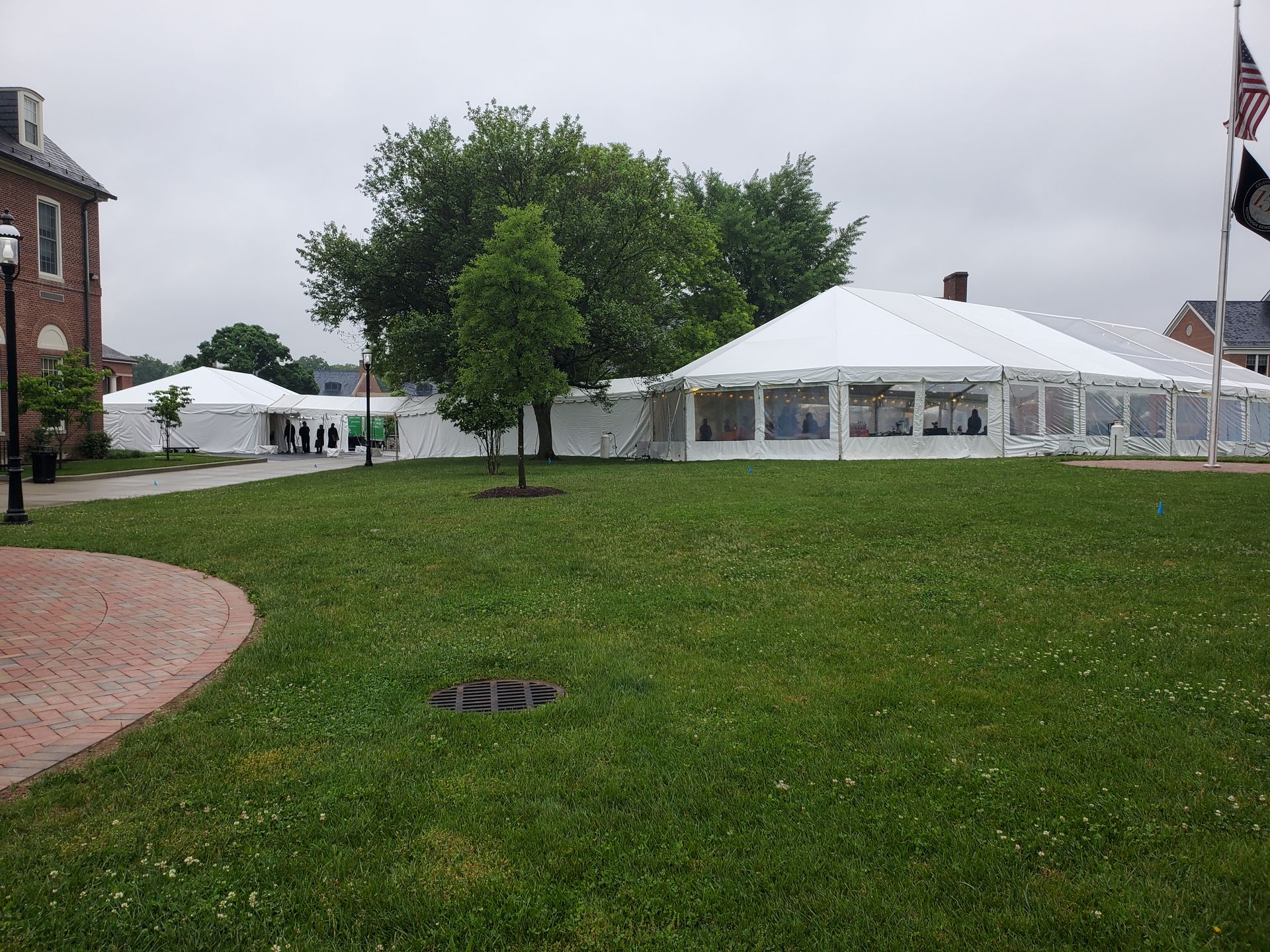 Tents set up on a green lawn, possibly for an event, with a building and flags in the background.