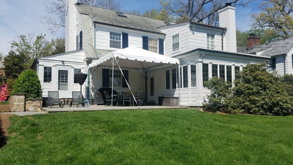 Backyard of a white house with a tent, green lawn, and outdoor furniture.