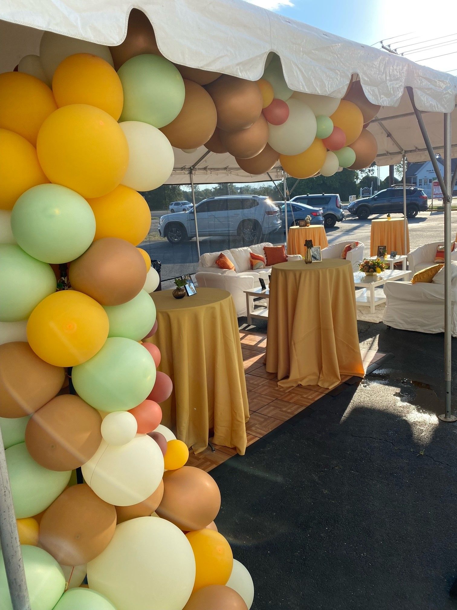 Balloon arch decorates an outdoor tented event with gold tablecloth tables.