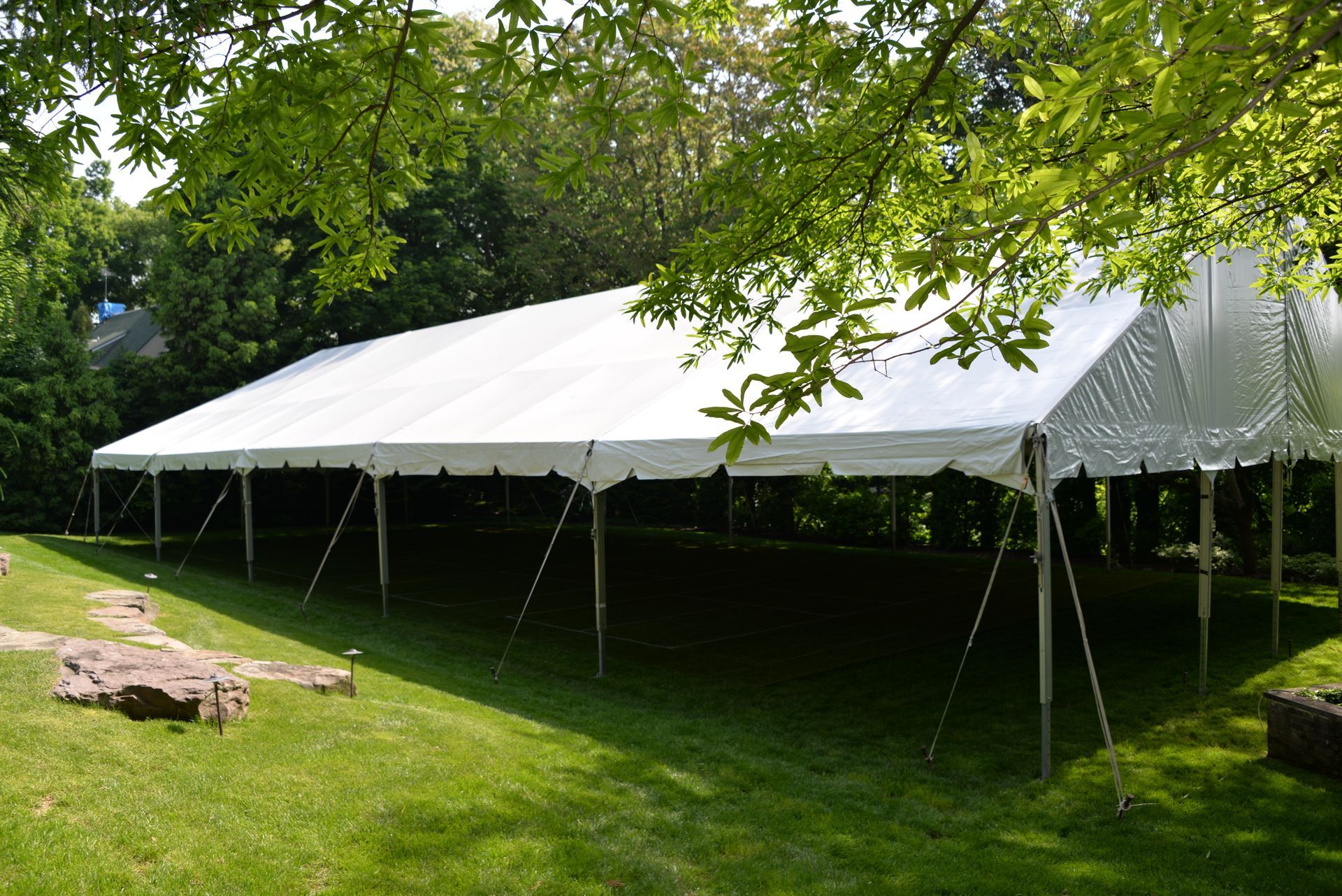 A large white event tent set up on a green lawn, with trees in the background.