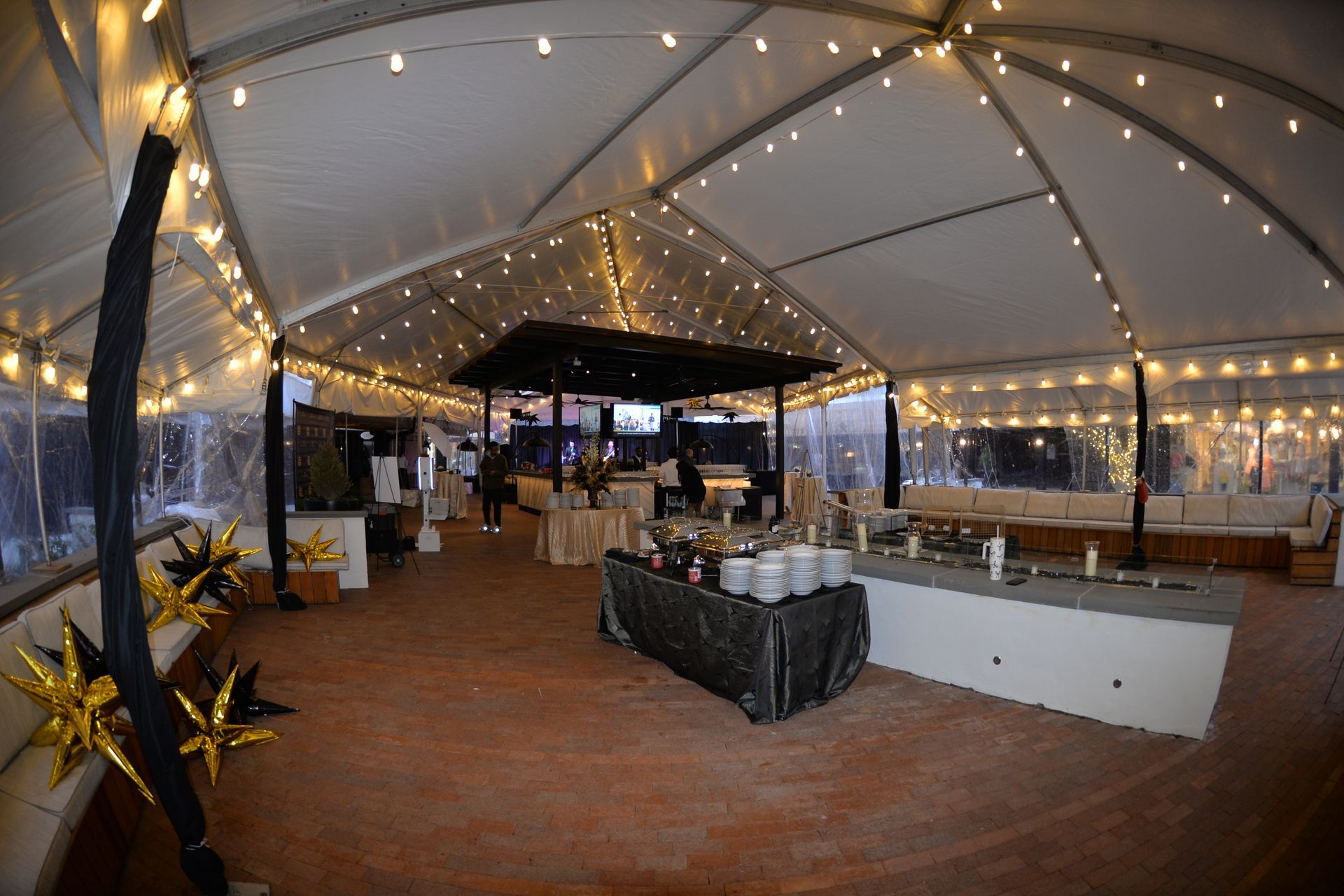 A tented event space with buffet tables, string lights, and a brick floor.
