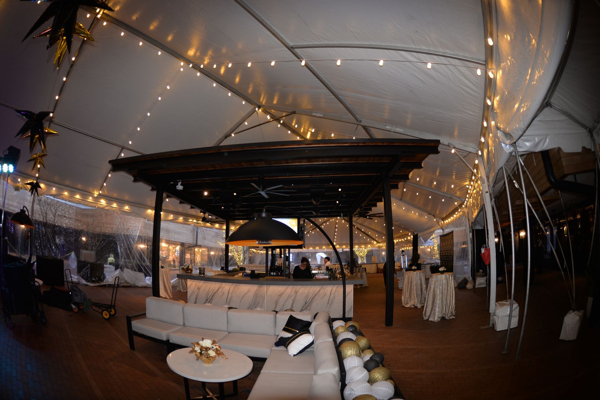 Inside a large tent with a bar, seating, and string lights.
